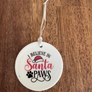A round wooden ornament with 'I believe in Santa Paws' text and paw prints.