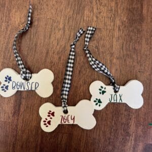 Three personalized dog bone-shaped tags on a wooden surface.