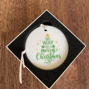 Round Christmas ornament with a festive message and holly decoration.